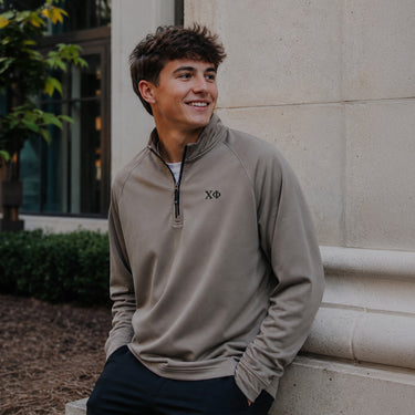 College-aged man wearing the Mushroom Cutter & Buck Adapt quarter-zip with black embroidered Chi Phi Greek letters outdoors on campus.