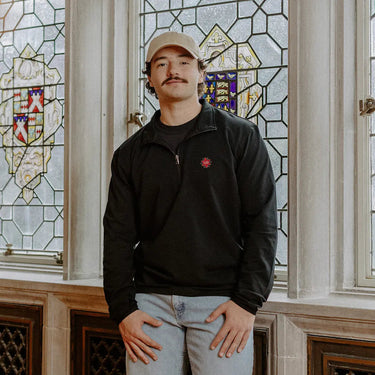 Male model wearing the black Chi Phi Embroidered Luxe Quarter Zip in front of stained glass windows with fraternity crests.